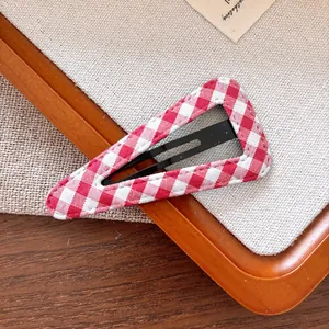 Gros plan d'une barrette BB à carreaux rouges et blancs sur un fond en tissu texturé