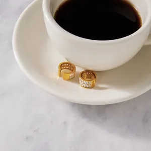 Détail de boucles d'oreilles en acier doré avec oxydes de zirconium près d'un café