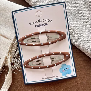 Dettaglio di due fermagli per capelli BB ovali a pois marroni su carta decorativa