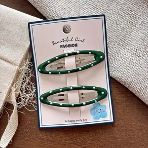 Dettaglio di fermagli per capelli ovali verde scuro a pois bianchi su supporto