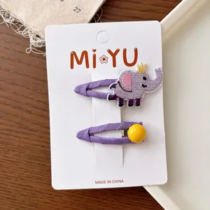Close-up of children hair clips featuring a purple embroidered elephant and a yellow bead
