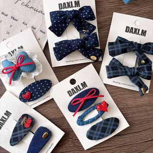 Detail view of navy plaid and denim hair clips with heart and cherry motifs on a display card