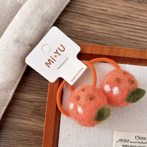 Vue détaillée d'élastiques à cheveux en feutre orange faits main sur tissu blanc et bois