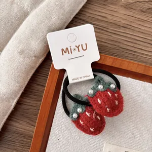 Détail d'élastiques fraises en laine feutrée rouge avec perles sur cadre en bois