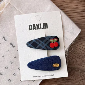 Close-up of navy plaid bow hair clip with cherry embroidery and handmade metal label