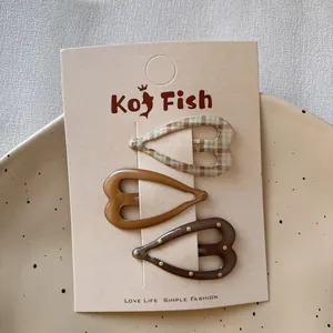Three-piece heart-shaped hair clip set in brown check and solid caramel colors on card