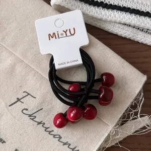 Set di tre elastici per capelli con ciondoli a ciliegia rossa su cartoncino bianco