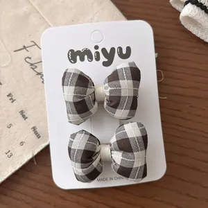 Détail de deux barrettes à nœuds à carreaux beige et marron sur carte de support