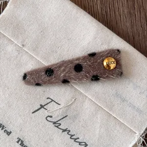Macro detail of brown plush hair clip with black dots and golden 'LUCK' metal button