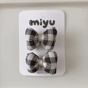 Détail de barrettes à nœuds à carreaux marron et crème sur une carte miyu blanche