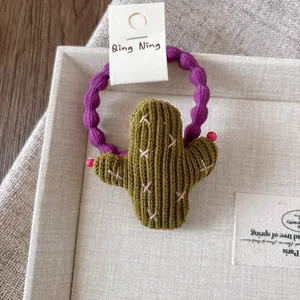 Detailed view of children's purple wavy velvet hair tie with a green knitted cactus charm