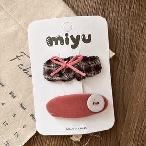 Detail view of pink velvet bow hair clip and brown plaid hairpin with white button