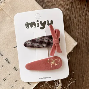 Detailed set of two pink velvet and plaid bow hair clips with embroidery on display card