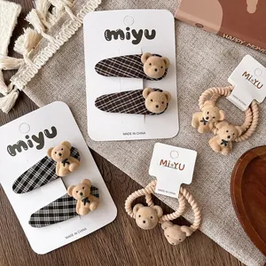 Detail of cute flocked bear hair clips and elastic ties with dark plaid pattern and beige fabric