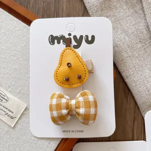 Detail of yellow pear leather clip and checkered bow hair accessory on a display card