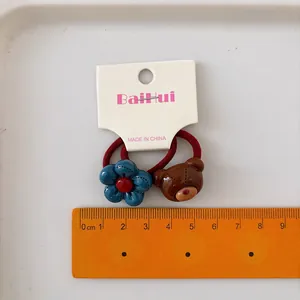 Set of two elastic hair ties featuring a blue flower and a brown cartoon bear for girls