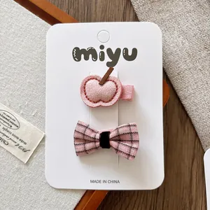 Detail of pink apple clip and plaid bow hairpins set on a branded white card packaging