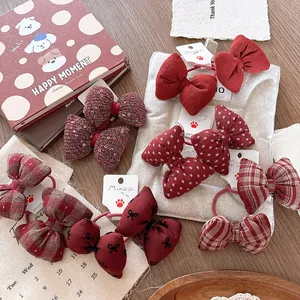 Detail of red bow hair ties featuring plaid, polka dot, and sequin patterns on a wooden desk