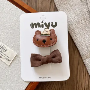 Detailed view of children's brown leather bear and fabric bow hair clips set