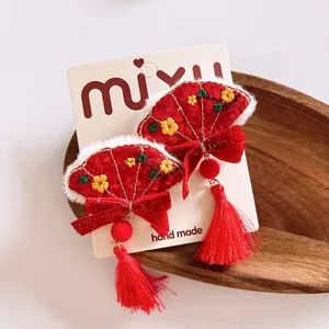 Detalle de pinzas para el cabello rojas en forma de abanico con bordado, piel y borlas