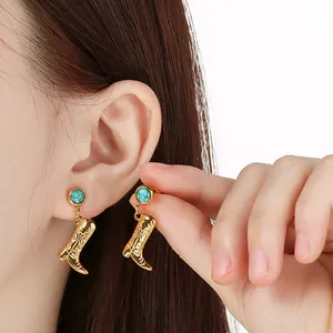 Close-up detail of stainless steel earrings with turquoise stud and golden cowboy boot