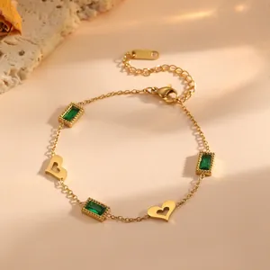 Detail van een goudkleurige armband met holle hartjes en smaragdgroene stenen.