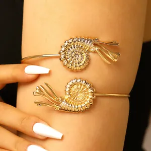Detailed macro view of a golden nautilus shell adjustable arm cuff worn on the arm.