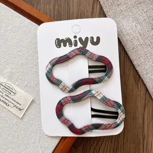 Détail de deux pinces à cheveux ondulées en tissu écossais rouge et vert sur carte miyu