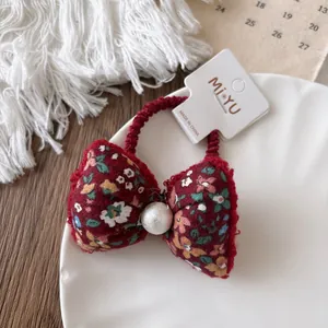 Detail of red floral velvet hair scrunchie with bow and pearl on a white ceramic plate