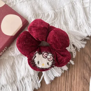 Macro detail of red corduroy scrunchie featuring cartoon embroidery and sparkling rhinestone