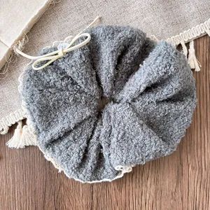 Close-up of grey plush hair scrunchie with lace trim and white button detail on fabric