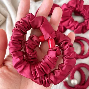 Dark red satin scrunchie with bow-tie accents and pleated silk texture held in hand