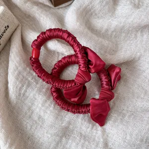 Close-up of wine red satin hair scrunchies with elegant bow and pleated texture