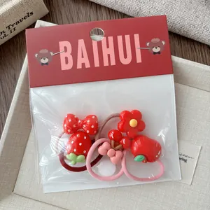 Detail of red cartoon hair ties for girls including strawberry and bow resin charms