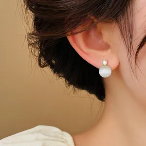 Elegant detail showing a round cat's eye stone stud earring with sparkling zircon worn on ear