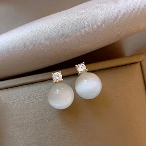 Elegant cat-eye stone stud earrings with zircon detail on gold jewelry box display.