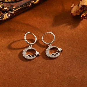 Detalle de pendientes plateados de luna e estrella con símbolo de infinito.