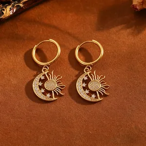 Detalle de pendientes de aro en acero dorado con sol y luna y detalles de cristal pavé