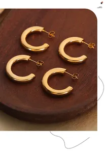 Detail von glänzenden goldenen C-förmigen Titanohrringen auf Seidenstoff mit Metallglanz