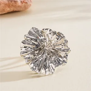 Close-up of a silver wrinkled flower ring with metallic texture on a beige background.