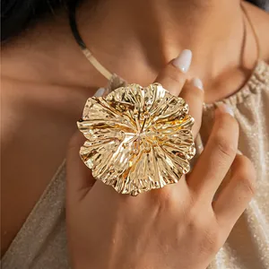 Close-up detail of an oversized gold metallic pleated flower ring worn on a hand