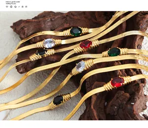 Detail von goldenen Titanstahl-Armbändern mit bunten ovalen Zirkonia-Steinen auf Holz