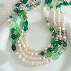 Collar artesanal con piedras naturales verdes y perlas de agua dulce sobre cerámica