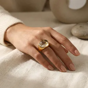 Primer plano de un anillo de acero dorado con una piedra de resina ovalada en la mano.