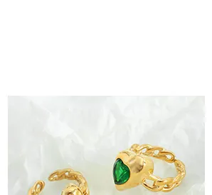 Macro detail of gold-plated chain ring featuring a green heart-shaped zirconia stone