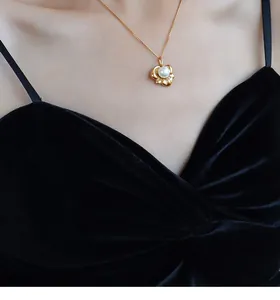 Detail der 18k vergoldeten Lotus-Halskette mit Perle auf elegantem schwarzem Kleid