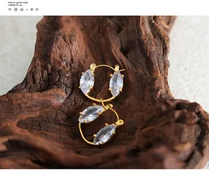 Detail view of gold hoop earrings with marquise-cut clear crystals on rustic wood background