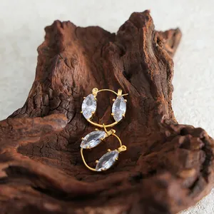 Golden titanium steel hoop earrings featuring marquise-cut zircons on a wooden background