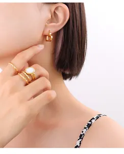 Detail view of gold 'D' earring and textured rings set with white stone on a model