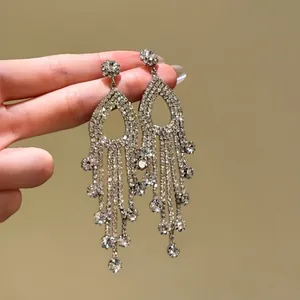 Macro detail of elegant silver needle drop earrings with sparkling rhinestones and long tassels.